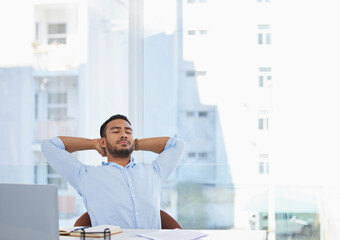 I deserve a break now. Shot of a young businessman sitting with his hands behind his head at his desk in an office.