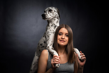 A young pretty woman is playing with her Dalmatian pet, isolated on a black background.