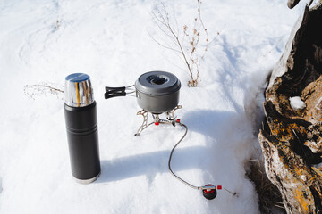 Utensils for cooking on a hike, camping equipment stands on the snow in winter. Cook the soup in a saucepan on a burner.