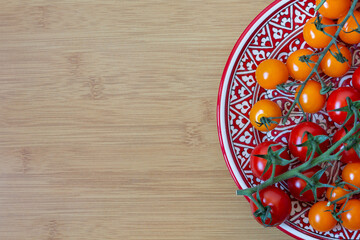 Flat-lay top-down still life with red and orange cherry-tomatoes on branch on plate on wooden table