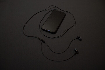 Black smartphone and earphones on a dark background still life