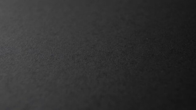 Black smooth paper surface. Macro. Rotation. Dark gray cardboard