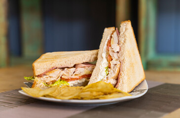 Chicken, mayonnaise, lettuce, tomato and bacon sandwich served with chips.