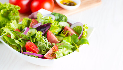 Fresh healthy vegetable salad made of cherry tomato, ruccola, arugula, feta, olives, cucumbers, onion and spices. Greek, Caesar salad in a white bowl on wooden background. 