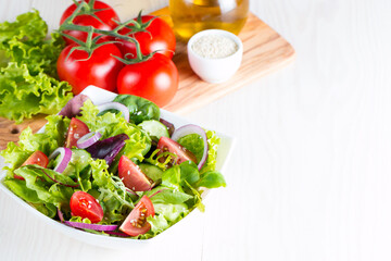 Fresh healthy vegetable salad made of cherry tomato, ruccola, arugula, feta, olives, cucumbers, onion and spices. Greek, Caesar salad in a white bowl on wooden background. 