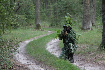 paintball sport player in protective uniform and mask aiming and shooting with gun outdoors of Forest