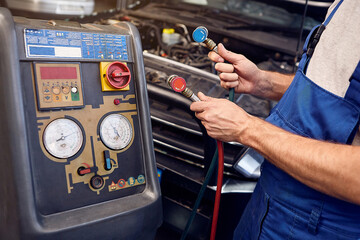 Mechanic holds a set of high-pressure pipes for filling the car's air conditioning system. A/C...