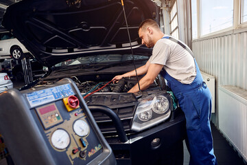 Mechanic pumps freon into the conditioning system on auto service