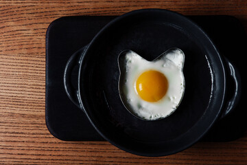 Fried eggs in the shape of a bear in a frying pan on a black wooden board. Top view
