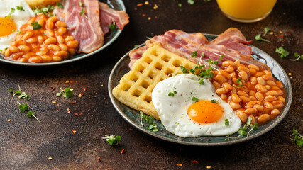 Potato waffles with fried egg, bacon and baked beans. Morning breakfast