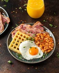 Potato waffles with fried egg, bacon and baked beans. Morning breakfast
