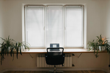 a wooden table from the windowsill, a working area on the windowsill, a laptop and an armchair by the window.