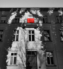A red duvet draped over a balcony on the top floor of a house in black and white