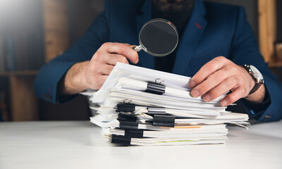 Businessman looking a magnifying glass to documents