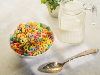 Colored fruit rings in a bowl, a spoon, a jug of milk and an indoor flower decor. Isolated on white background. Quick whole grain breakfast. Children's, diet food. Healthy lifestyle. Banner.