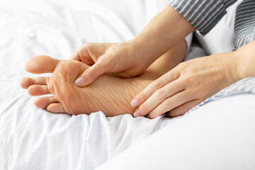 Woman does self massage of her foot and relaxes at home. Close-up of a female hands pressing massage points. Painful legs from wearing uncomfortable tight shoes and high heels, fatigue and tension.