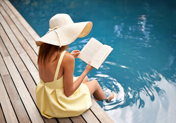 Summer vacation with a great book. young woman relaxing at the pool with a book.