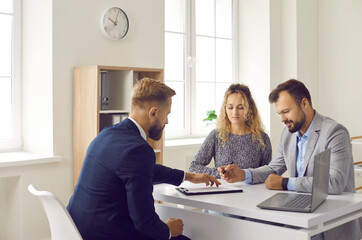 Happy Caucasian couple buyers sign paper contract make deal with male real estate agent in office....