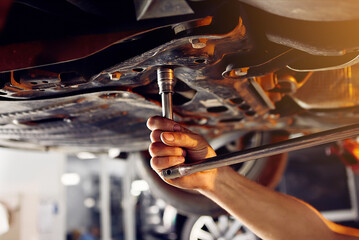 Auto mechanic checking running gear of automobile on service station. Male worker fixing problem with car. Vehicle maintenance concept