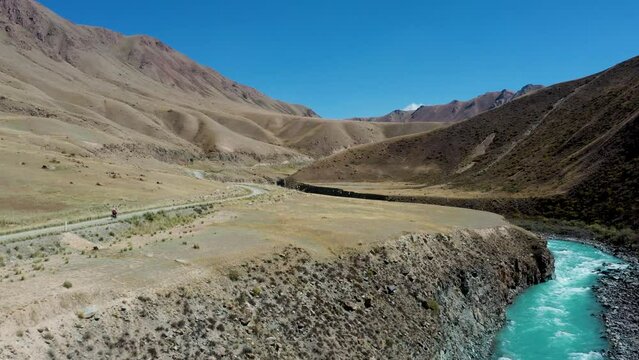 Aerial over offroad motorcycle rides on a gravel path near arid desert mountains. Travel along the Silk Road along the Pamir Highway in the desert of Kyrgyzstan and Tajikistan, Central Asia. 4K drone