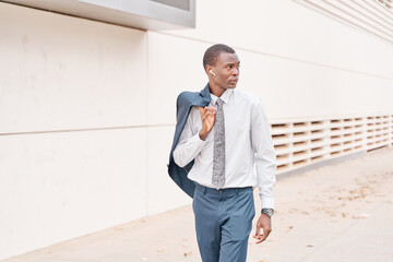 african-american businessman walking with his jacket over his shoulder and listening to music.