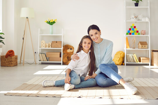 Portrait of mother and child. Happy family spending time at home. Mom and kid posing for photo. Beautiful single mum together with preteen daughter sitting on floor in cozy light spacious living room