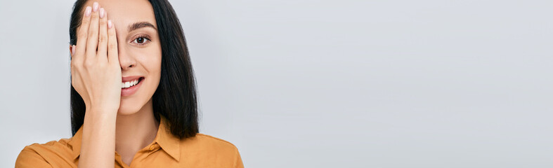 Woman closing eye with her hand for checking vision, isolated on grey background. Vision test concept for adult © Peakstock