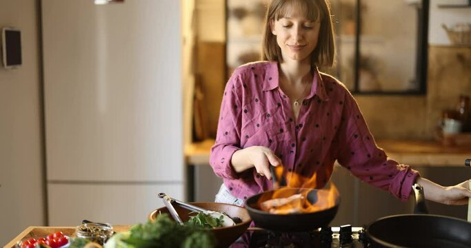 Young woman mixing salad and frying salmon steaks, cooking healthy food in the kitchen at home. Healthy lifestyle and wellness concept