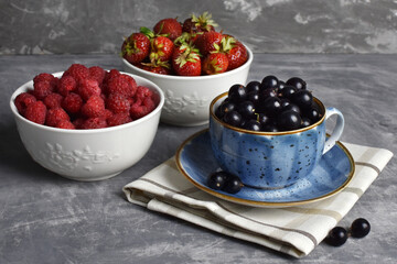 ripe berries currants strawberries raspberries in bowls on a gray background