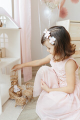 Six year girl wearing light pink dress play with miniature furniture for doll house at home