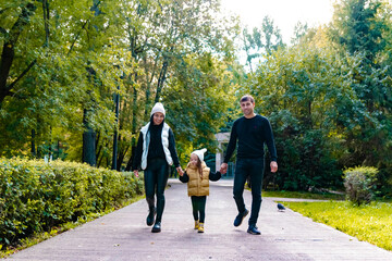 Obraz premium A woman and a man and a child are walking in the park. Summer park. Green trees. The concept of a young family.