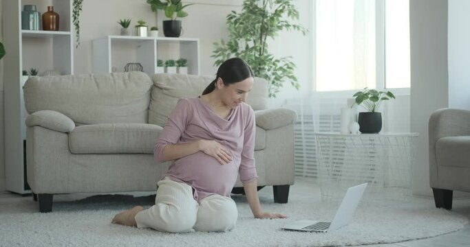 Pregnant woman exercising watching video tutorial on laptop at home
