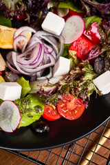 Fresh greek salad with tomato, radish, onion, bel pepper , olives and feta cheese on black plate, side view, wooden background