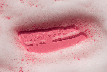 Fototapeta premium Foam on a pink background. Soapy liquid texture with bubbles. Natural sunshine and shadows. Skincare cleansing cosmetic in top view.