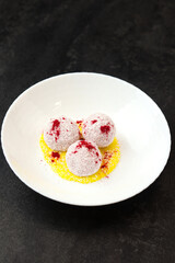 Homemade coconut balls, raw and healthy sugar free rafaello candies. Vegetarian energy sweets recipe. Round tasty dessert in bowl with yellow mango sauce on dark background. Copy space, close up view.