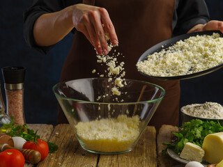 Grated cheese in a glass bowl in frozen flight on a dark background. Vegetables, herbs, eggs, spices on a wooden table. A professional chef prepares grated cheese dishes. Close-up.