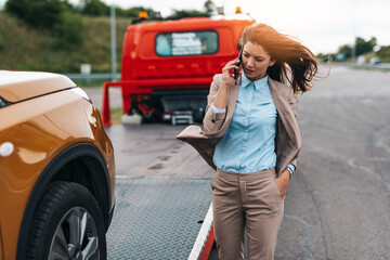 Elegant middle age business woman calling someone while towing service helping her on the road....