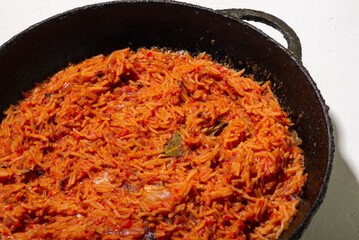 Jollof rice in a frying pan on a white background. A traditional Nigerian dish of rice, tomatoes and spices.