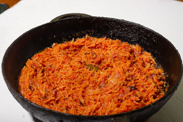 Jollof rice in a frying pan on a white background. A traditional Nigerian dish of rice, tomatoes and spices.