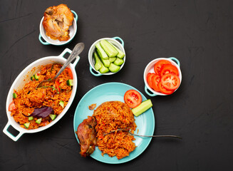 Jollof rice with chicken meat on a plate. Rice with tomatoes, onions, spices. Traditional national Nigerian food. Dark background.