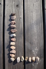 Letter L from small river stones. Capital letter on wooden background. Stone alphabet.