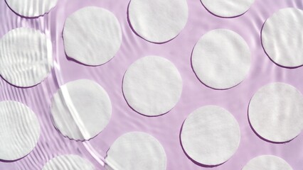 Top view of water ripples and waves over cotton pads arranged in rows on purple background | Beauty...