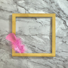 One pink feather in a gold frame. Gray white marble background. Text space. Top view. Minimal style.