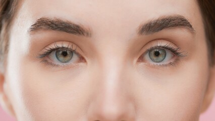 Extreme close-up beauty portrait of young European woman with brown hair looking at the camera against pink background | Skincare commercial concept