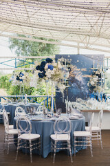 Coziness and style. Modern event design. Table setting at wedding reception. Floral compositions with beautiful flowers and greenery, candles, laying and plates on decorated table.