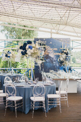 Coziness and style. Modern event design. Table setting at wedding reception. Floral compositions with beautiful flowers and greenery, candles, laying and plates on decorated table.