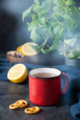 Red  cup of tea with lemon, mint and salt cracker on dark background. The concept of mood breakfast
