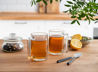 Two cups of tea with lemon and dry herbal flowers on a wooden countertop against the background of a white kitchen in the early morning. Healthy breakfast concept