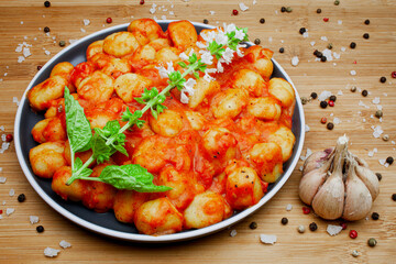 Traditional homemade Italian gnocchi in aromatic tomato sauce served on a decorative plate and garnished with herbs, basil, colored pepper, garlic and pink Himalayan salt. 