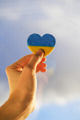a man holds a heart in the color of the flag of Ukraine against the blue sky. war in Ukraine